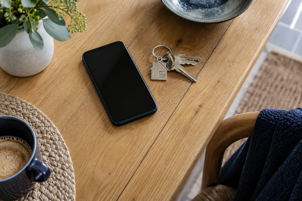 An overhead view of a plain smartphone and house keys on oak